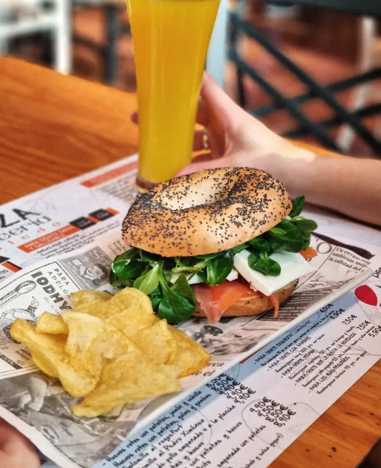 Bagel de salmón con canónigos y queso fresco, con patatas chips, sobre el mantel de papel de La Tiza.