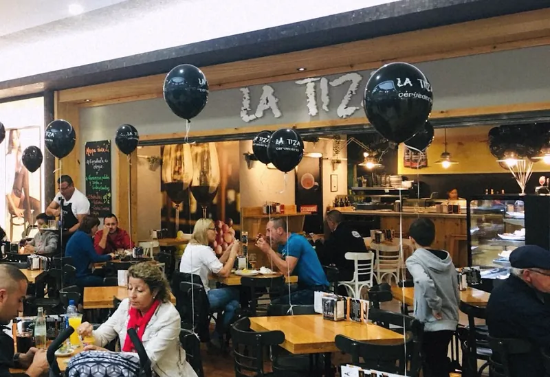 El local de La Tiza desde el pasillo del centro comercial, con globos negros con el logo y las mesas llenas.