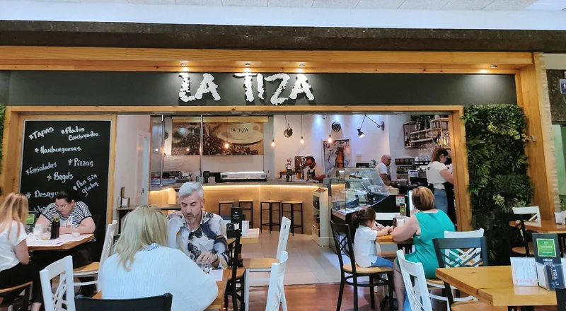 La entrada de La Tiza en el Centro Comercial Rosaleda: el rótulo LA TIZA, la pizarra con la oferta del día, la barra y las mesas con clientes.